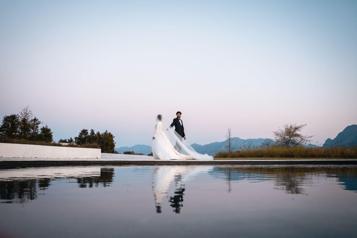 Bride and groom reflected in a still pool at dusk beneath the Winelands mountains